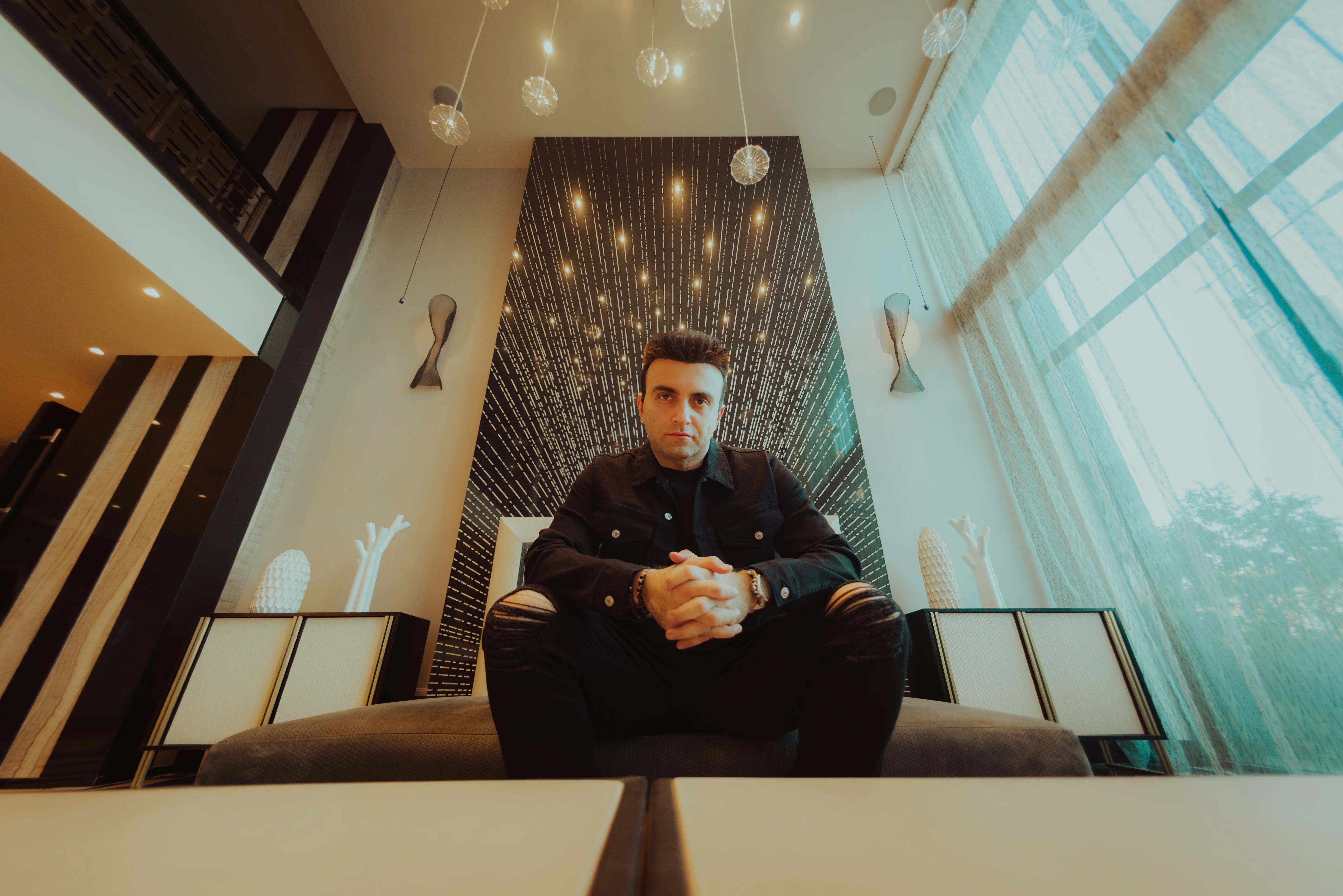 Taha Asadi seated on a sofa in a high-ceilinged lobby, hands clasped, looking into the camera